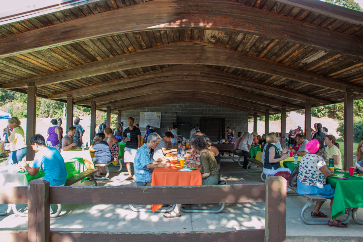 A photo of a group of people sitting under an outdoor gazebo, eating plates of food.