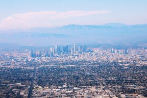 A photo taken from a plane overlooking the Los Angeles skyline, which appears in vivid pink and blue hues.