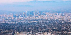 A photo taken from a plane overlooking the Los Angeles skyline, which appears in vivid pink and blue hues.
