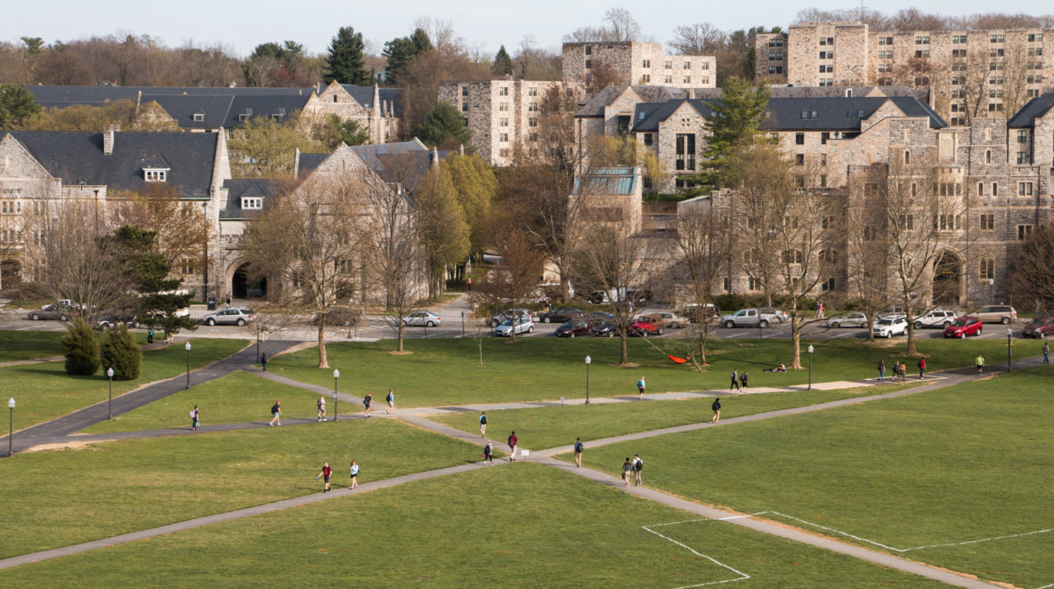 A photo overlooking a green lawn on a college campus with several gray buildings in the background.