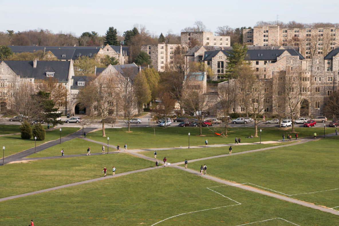 A photo overlooking a green lawn on a college campus with several gray buildings in the background.