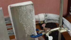 Image of an aluminum slab set up in a lab space with chunks of melting frost dripping off.