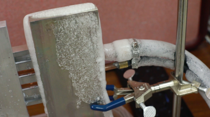 Image of an aluminum slab set up in a lab space with chunks of melting frost dripping off.