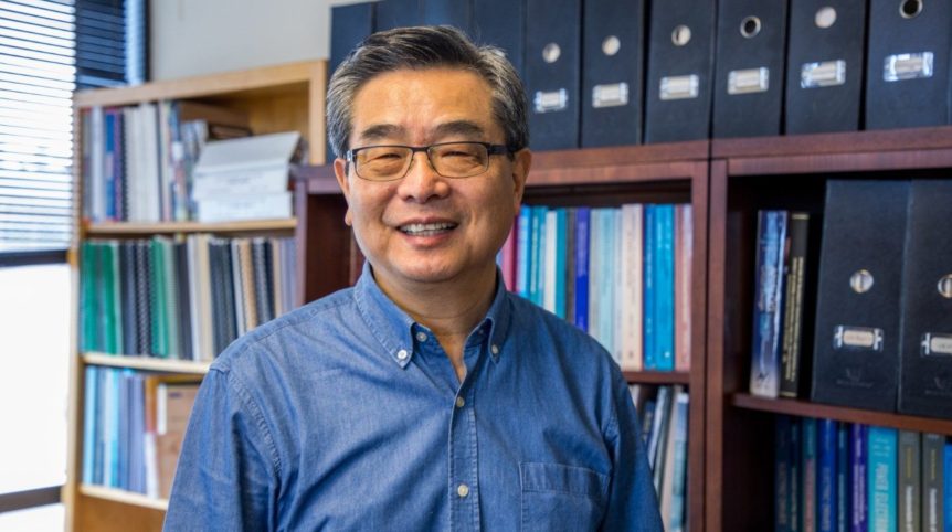 A portrait of Fred Lee in his office, in front of full bookshelves.