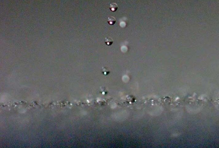 An image of water droplets jumping off of a surface.