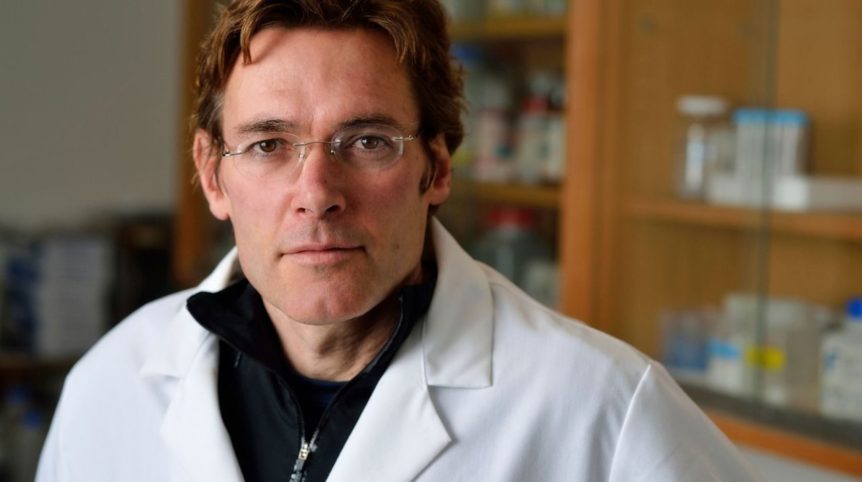 A man, Marc Edwards, poses for a portrait. He is in a lab, wearing a white lab coat.