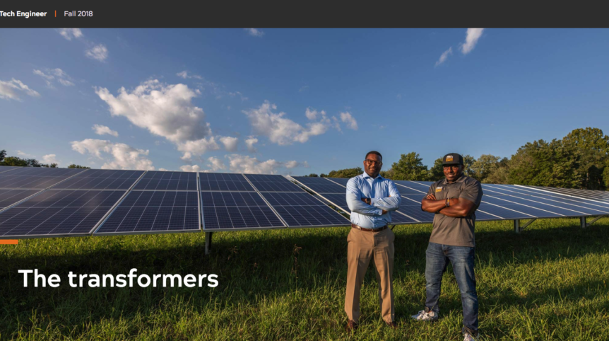 Screenshot of a photo in which two men pose in front of solar panels in a field. The words "The transformers" are written on top of the image.