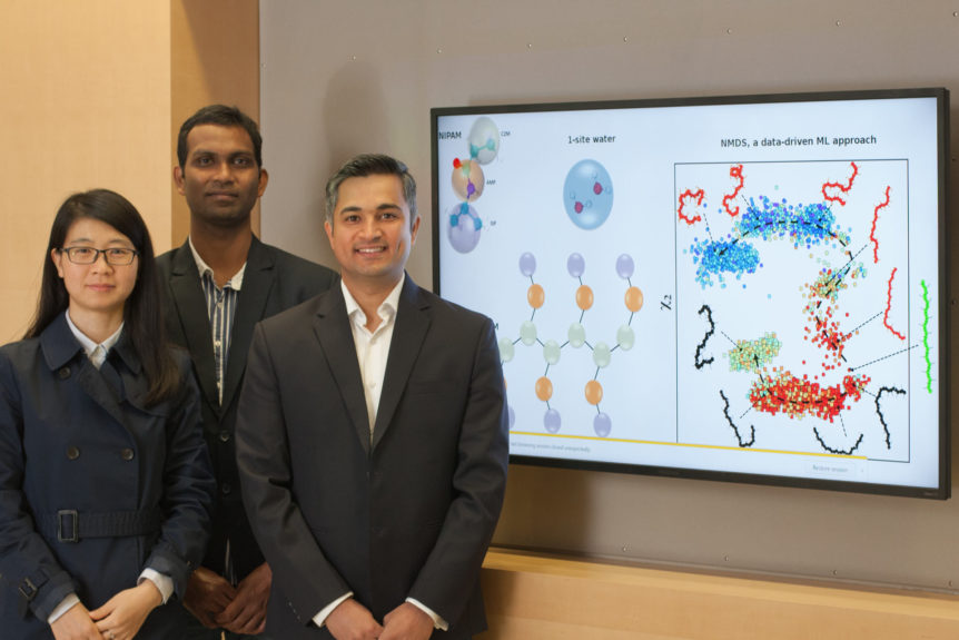 Three researchers pose in front of a screen displaying their research.
