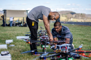 Two students adjust parts of a drone on the ground.
