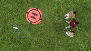 An overhead photo of three students flying a drone in a grassy field.