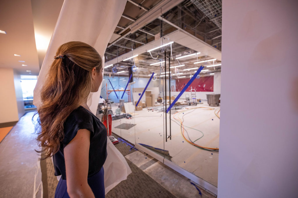 A young woman pulls a curtain back to reveal a lab space under construction.