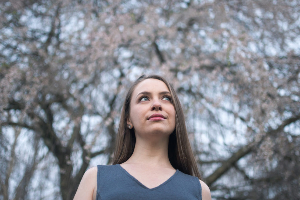 A photo of a young woman with blue eyes looking off in the distance, with a backdrop of cherry blossoms.
