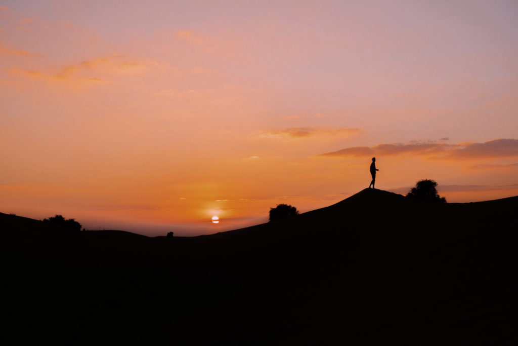 A photo of a desert sunset, with a man's silhouette atop a peak.