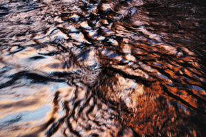 A photo of ripples of a river bathed in sunset hues of pinks and blues.