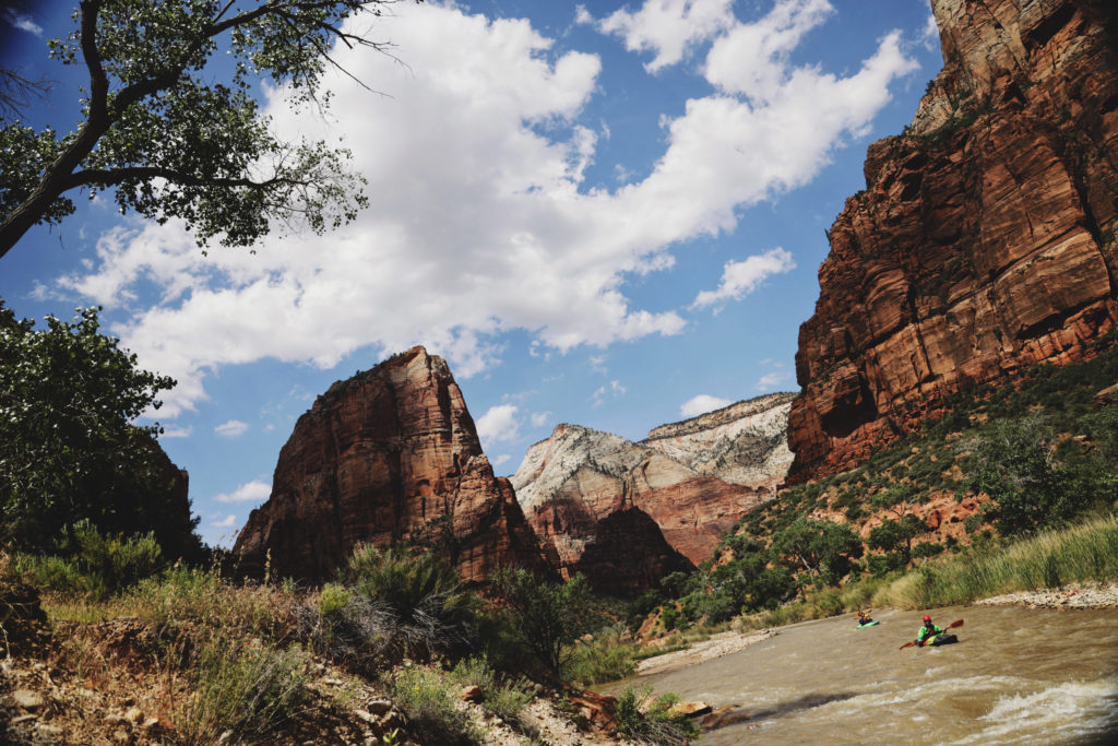 A photo of Zion National Park with the Virgin River flowing through it. Two kayakers are floating through the river.